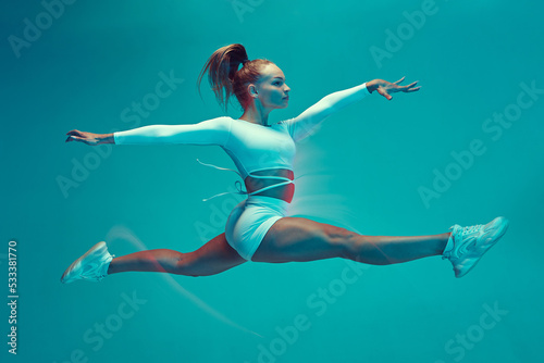 A beautiful girl in a white sports uniform does the splits in a jump. Dancing, sports, grace, stretching.