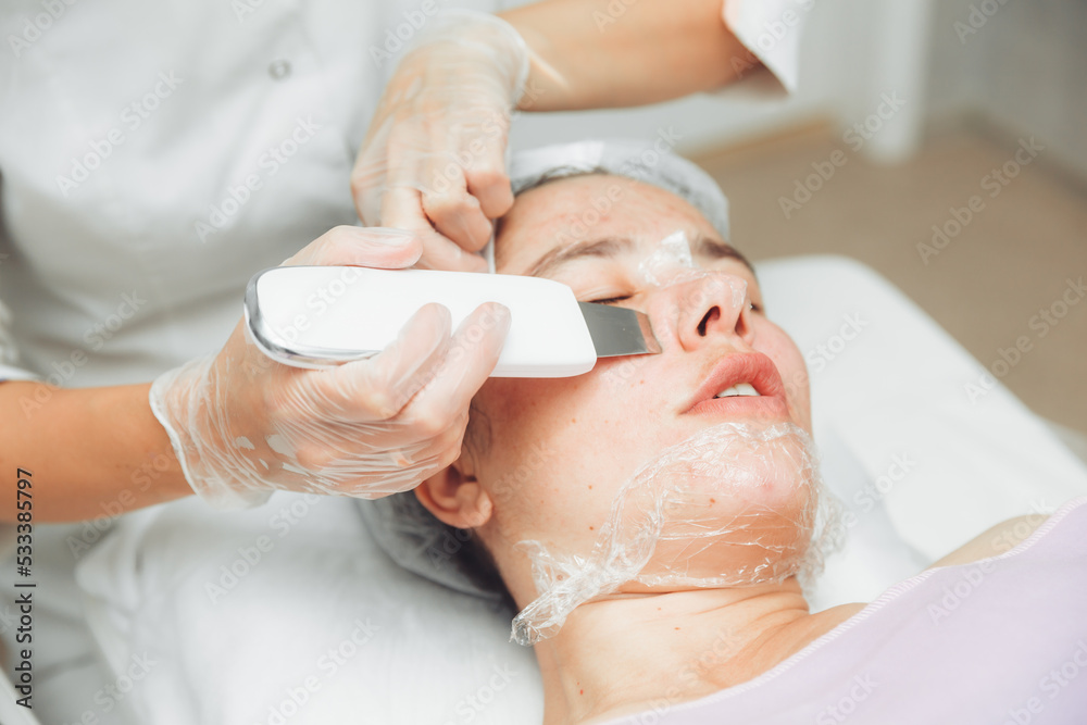 Ultrasonic cosmetic scrubber. Facial cavitation procedure. Salon skin care procedure. Professional hardware peeling. Acne removal. contaminated person Ultrasonic cosmetic scrubber. Facial cavitation procedure. Salon skin care procedure. Professional hardware peeling. Acne removal. contaminated person