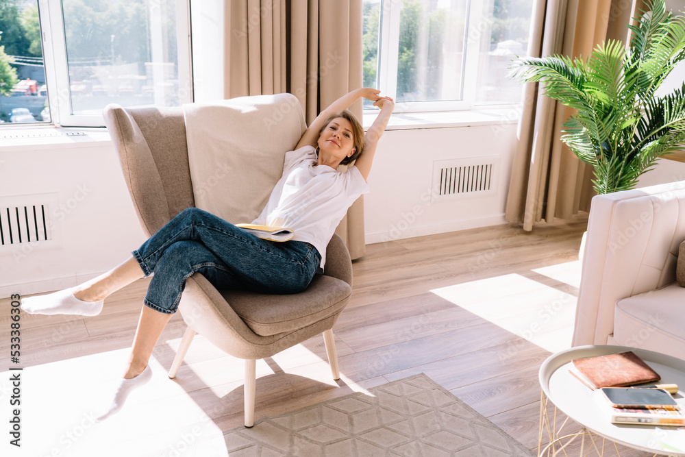 Relaxed woman sitting on chair raising arms at home Relaxed woman sitting on chair raising arms at home