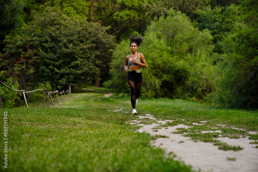 Fototapeta premium Young black woman in sports wear running at summer park