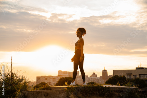 Black runner woman standing in summer park on sunrise