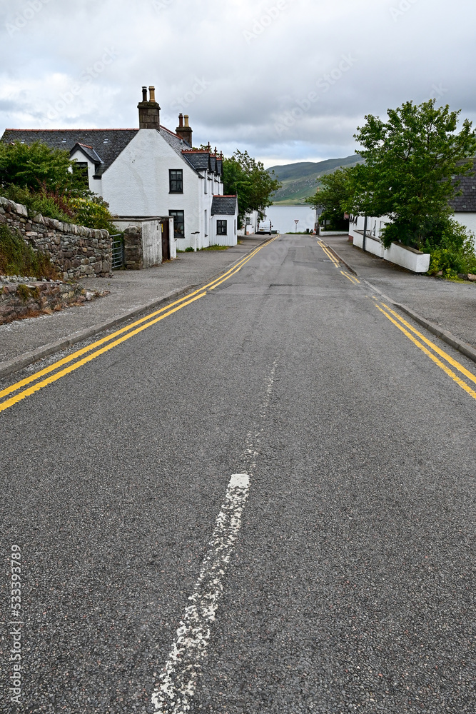 Empty road with yellow and white paint lane markings with a pavement and a house wall in Ullapool, Highland, Scotland