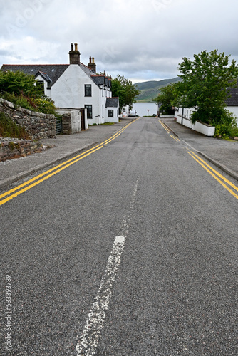 Empty road with yellow and white paint lane markings with a pavement and a house wall in Ullapool, Highland, Scotland photo