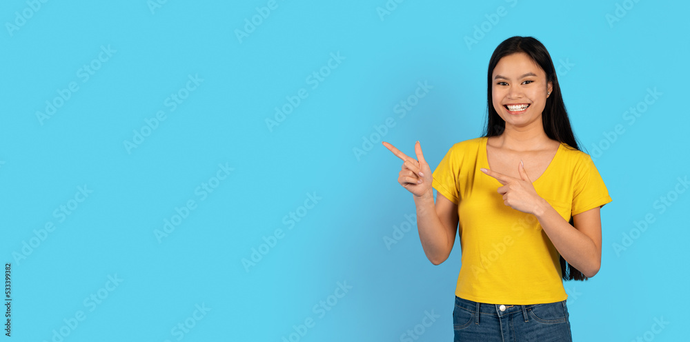 Great ad and offer. Smiling inspired young korean woman in yellow t-shirt pointing fingers at empty space Great ad and offer. Smiling inspired young korean woman in yellow t-shirt pointing fingers at empty space