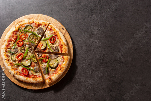 Vegetarian pizza with zucchini, tomato, peppers and mushrooms on black stone. Top view. Copy space