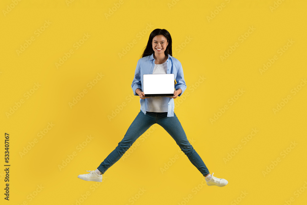 Smiling young chinese woman student in casual jumping, showing laptop with blank screen Smiling young chinese woman student in casual jumping, showing laptop with blank screen