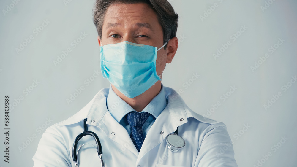 doctor in white coat and medical mask looking at camera isolated on grey. doctor in white coat and medical mask looking at camera isolated on grey.