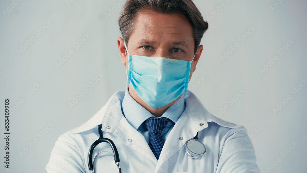 doctor in medical mask and white coat looking at camera on grey background. doctor in medical mask and white coat looking at camera on grey background.
