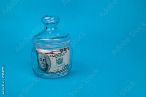 Glass jar filled with US dollar bill to display savings. On a blue background
