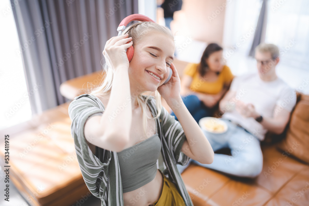 Happy young girl uses headphones to listen to music while relaxing at home with her family, and a gorgeous smiley woman enjoys her pastime and leisure time in the entertainment room. - obrazy, fototapety, plakaty 