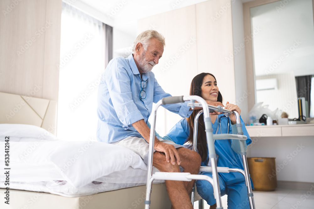 Fototapeta premium Portrait of Asian young nurse helping old elderly disable man grandfather to walk by using walker equipment in the bedroom. Senior patient of nursing home moving with walking frame and nurse support