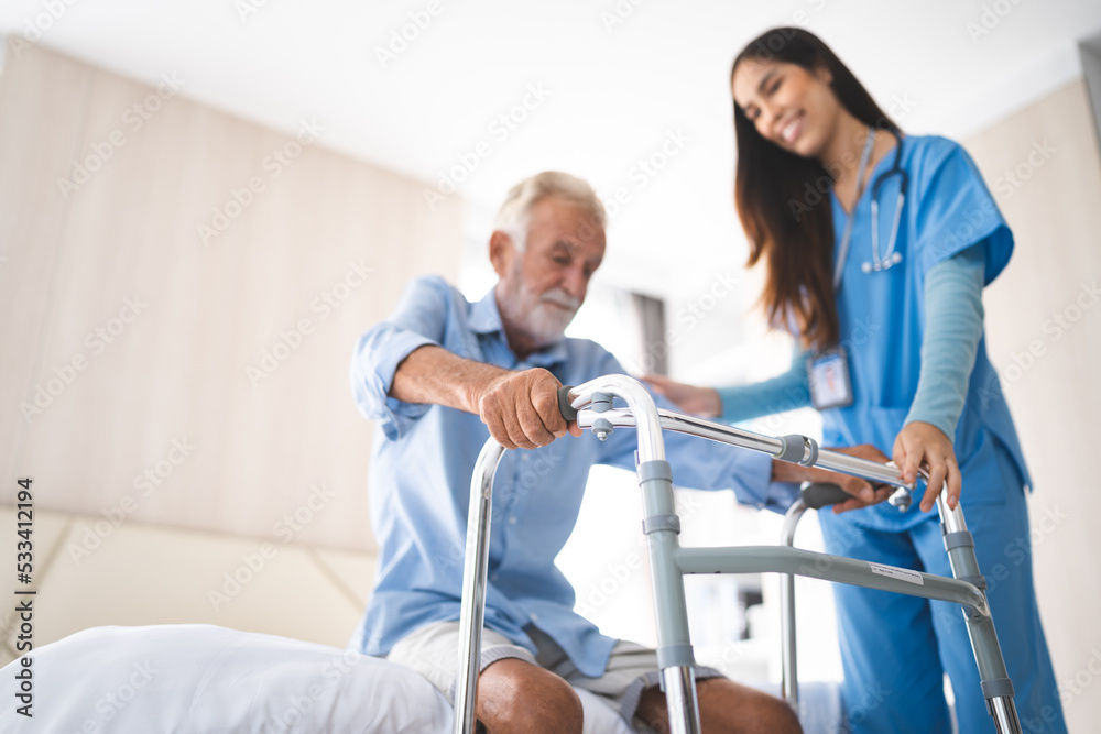 Fototapeta premium Portrait of Asian young nurse helping old elderly disable man grandfather to walk by using walker equipment in the bedroom. Senior patient of nursing home moving with walking frame and nurse support