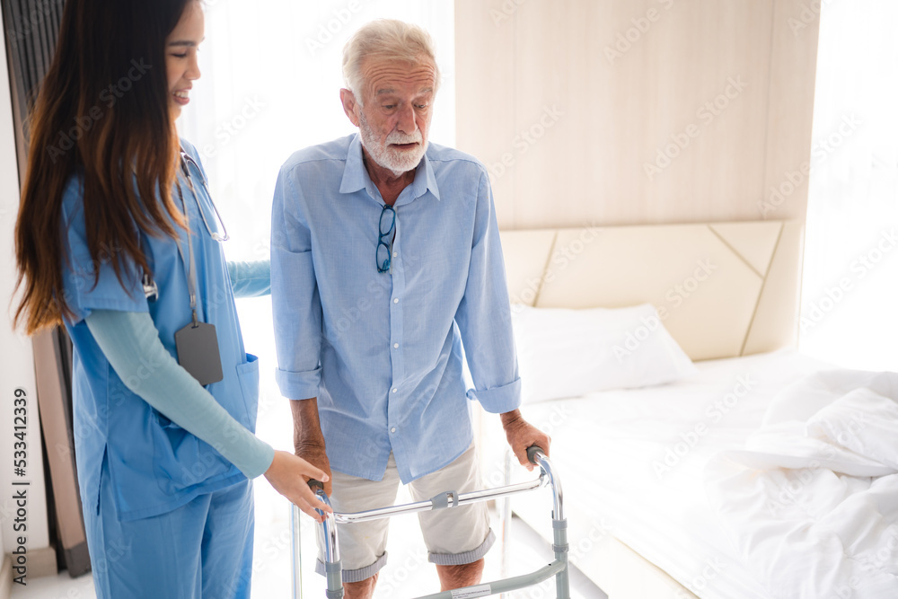 Obraz premium Portrait of Asian young nurse helping old elderly disable man grandfather to walk by using walker equipment in the bedroom. Senior patient of nursing home moving with walking frame and nurse support