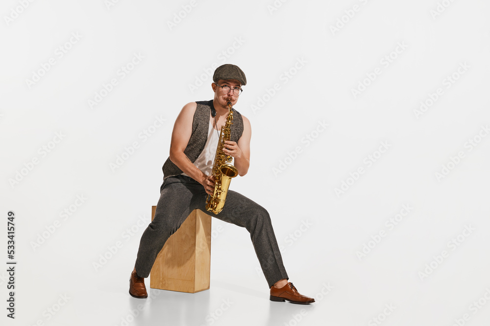 Naklejka premium Young musician in retro style outfit playing saxophone isolated over white studio background. Concept of music, hobby, festival.
