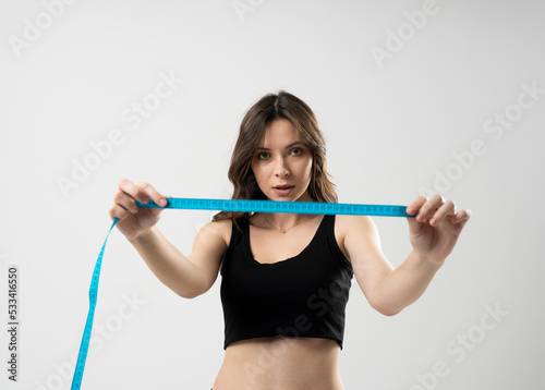 A body centimeter in the hands of girl in underwear after a workout or fitness session. Measurement of body volume. Healthy lifestyle, physical activity. Controlling figure while dieting. © Volodymyr