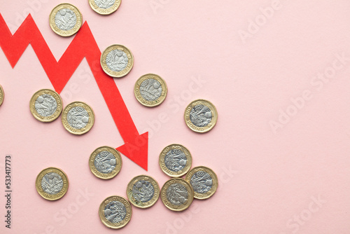 British pound sterling coins with a red downward arrow. Uk economic crisis