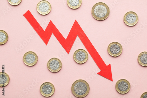 British pound sterling coins with a red downward arrow. Uk economic crisis