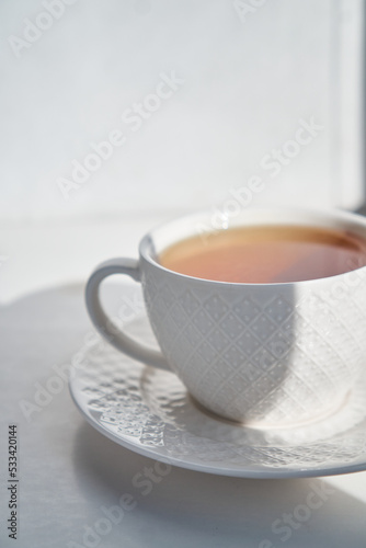 breakfast concept. white cup of tea couple coffee on white background, sunlight morning, hard shadows. side view, vertical photo, copy space, minimalism