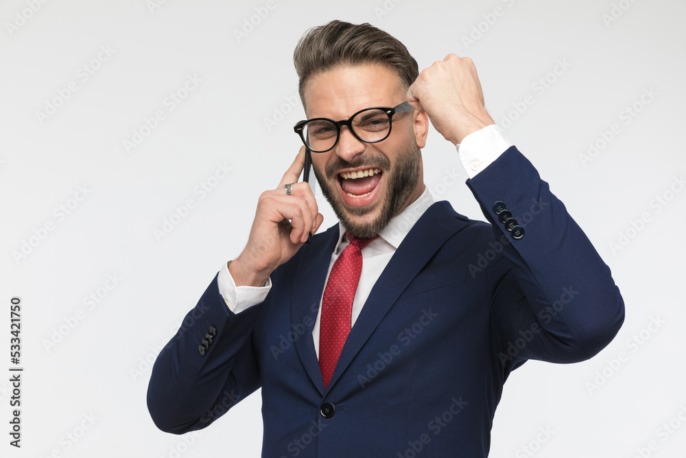 enthusiastic young man with glasses talking on the phone and celebrating enthusiastic young man with glasses talking on the phone and celebrating
