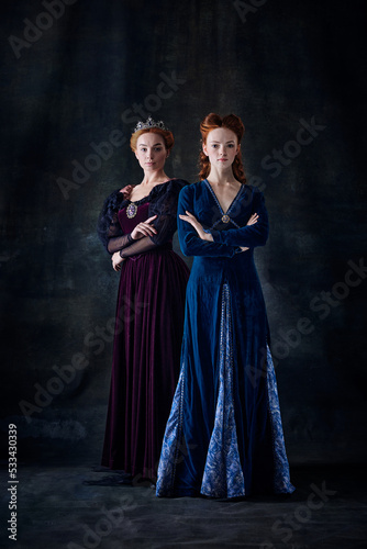 Portrait of two beautiful women in image of queen and princess isolated over dark background. Royal family