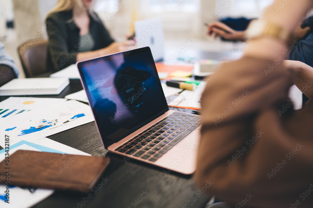 Crop employee working on laptop among colleagues