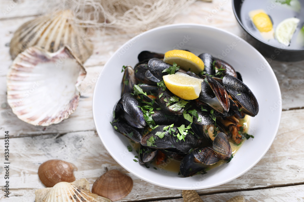 Mussels in wine-butter sauce, sprinkled with parsley, top view. Clams in a bowl, on white wood background. Mussels in wine-butter sauce, sprinkled with parsley, top view. Clams in a bowl, on white wood background.