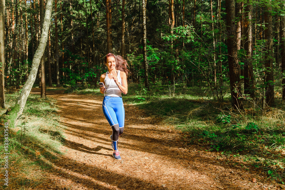 Young pretty woman running in the park at summer morning.The girl is listening to music while running.Sport and health nature concept