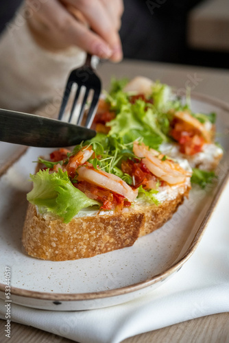 Sandwich, bruschetta with shrimp, fresh salad and sweet and sour sauce in a restaurant serving. The girl cuts a shrimp sandwich.