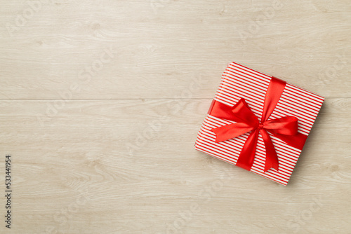 Gift box with red ribbon bow on wooden background, top view