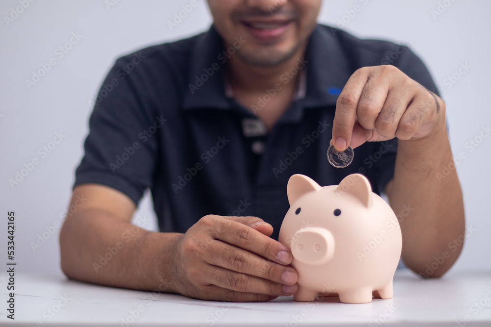 man putting coin in piggy bank and press the calculator with coins placed on the account book money saving concept man putting coin in piggy bank and press the calculator with coins placed on the account book money saving concept