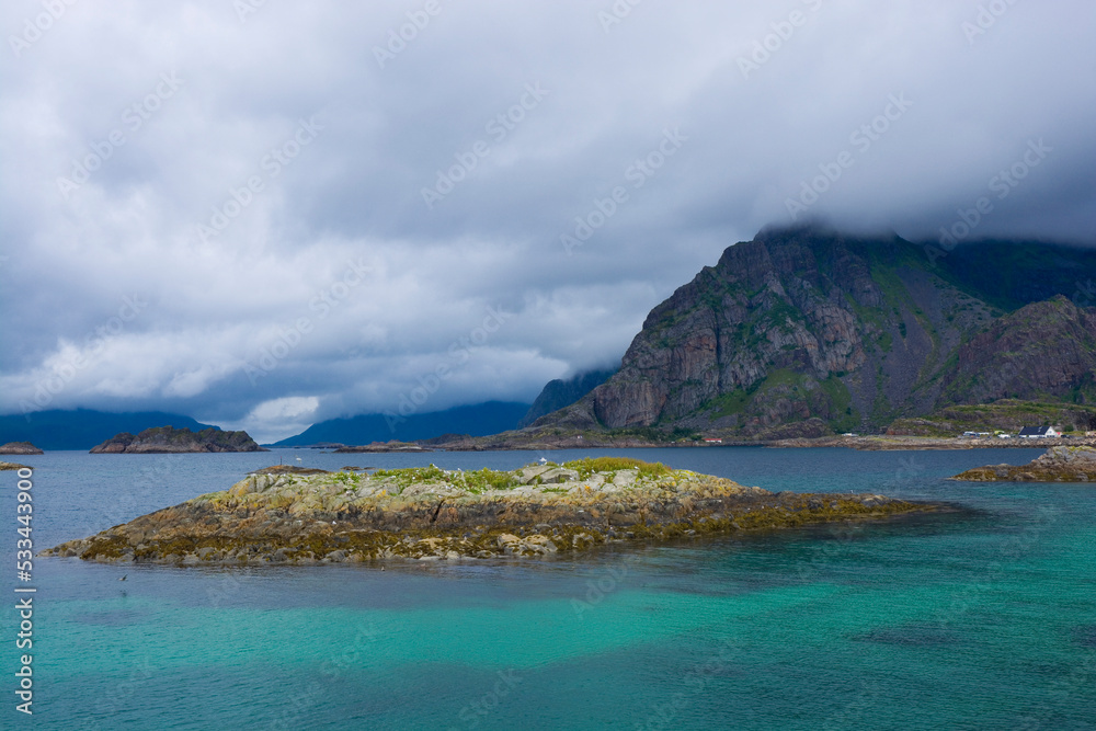 Birds island surrounden by turquoise water against cloudy sky, Lofoten, Henningsvaer, Norway