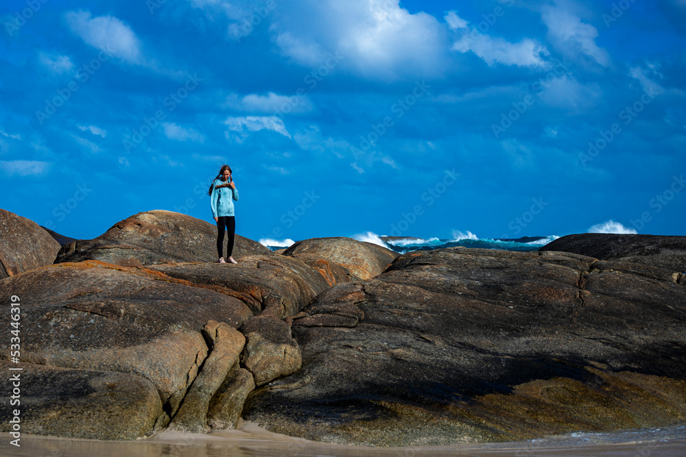 girl in ponytails walking along beach with massive rocks in the background, elephant rocks in western australia