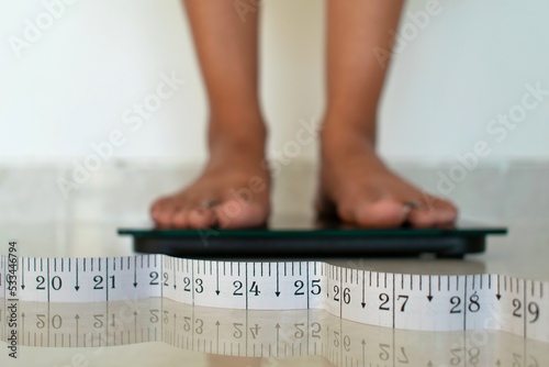 Woman feet standing measuring on weighing scales with tape measure result. Weight loss, weight gain, slim, body, fit,  healthcare, balanced healthy nutritious diet control lifestyle wellness concept