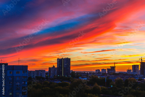 Red sunset and blue sky with a view of the houses in the city. Tower cranes and houses under construction in the city at sunset. A bright red sunset with heavy dark clouds. Impending disaster.