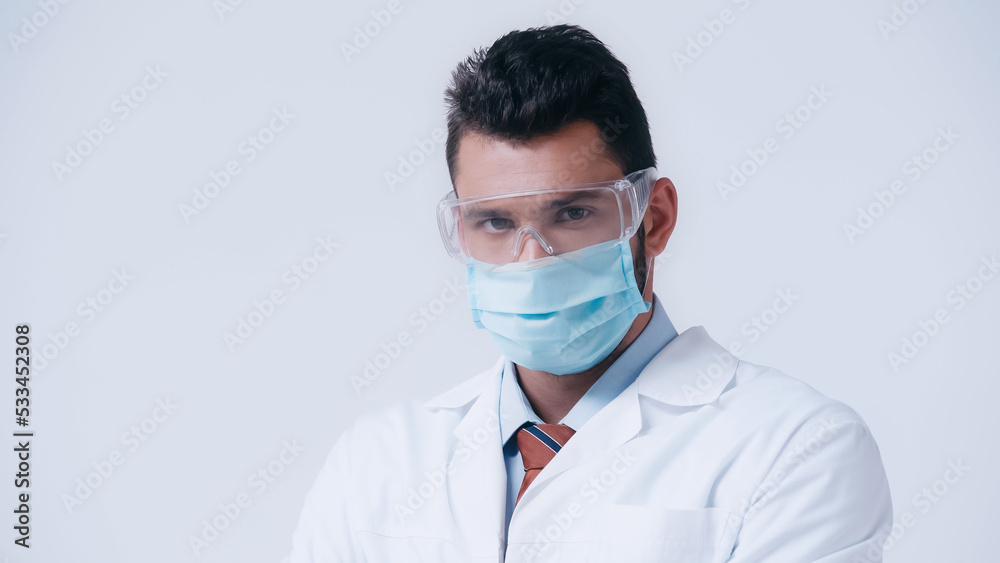 brunette scientist in medical mask and goggles looking at camera isolated on grey. brunette scientist in medical mask and goggles looking at camera isolated on grey.