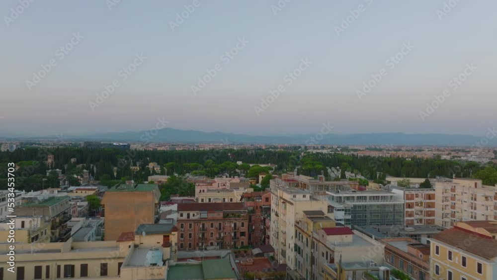 Low flight above apartment buildings in city at dusk. Revealing large park with Verano Monumental Cemetery. Rome, Italy Low flight above apartment buildings in city at dusk. Revealing large park with Verano Monumental Cemetery. Rome, Italy