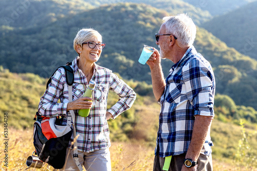 Two senior adult have pause on hiking and drink water and smile in natural environment