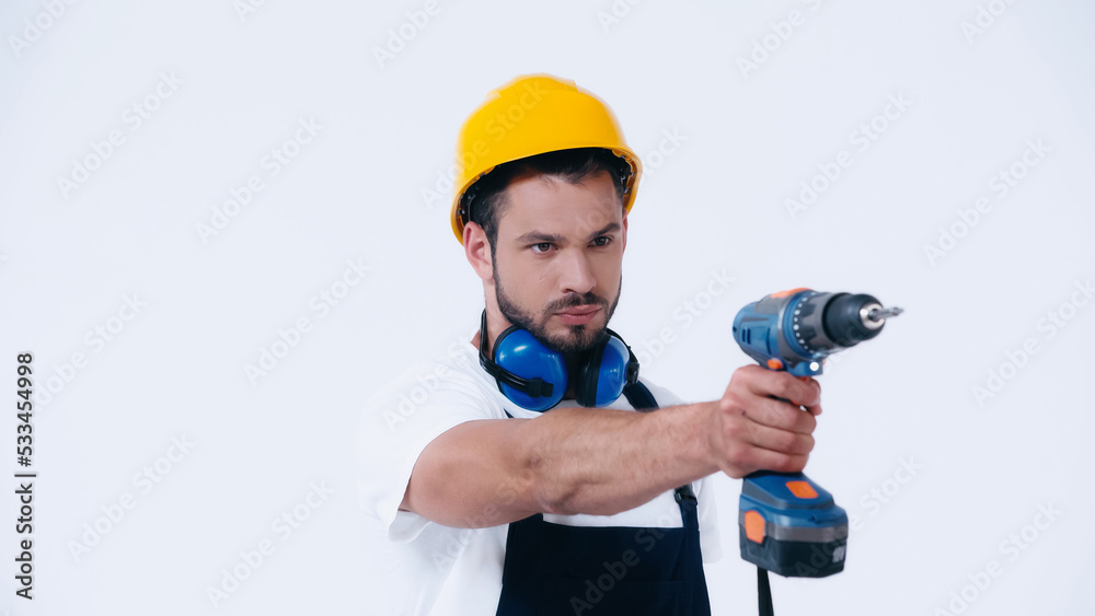 serious handyman in protective helmet working with electric drill isolated on white. serious handyman in protective helmet working with electric drill isolated on white.