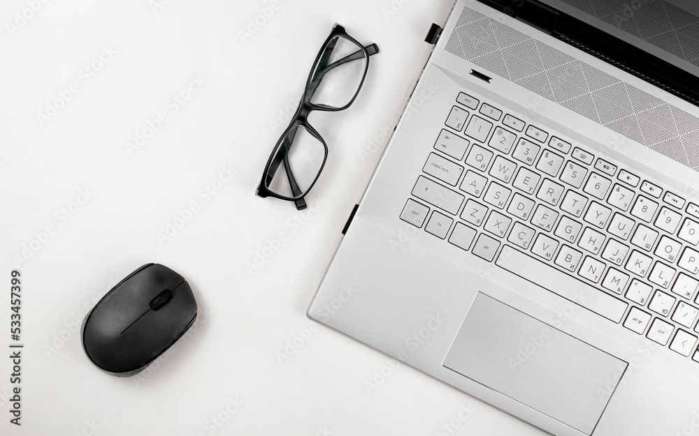 A laptop with glasses and computer mouse are on a white table. Top view with copy space A laptop with glasses and computer mouse are on a white table. Top view with copy space