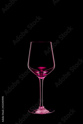 Empty wine glass backlit with bright pink light and isolated on black background. Beverage glassware concept. Copy space.