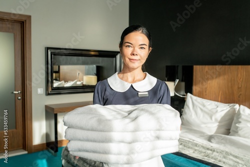 Photo realistic digital collage of happy room service staff holding stack of white clean sheets in bedroom