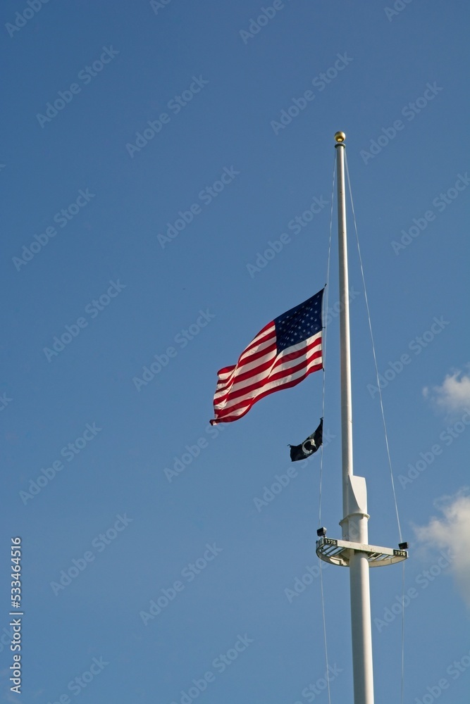 American flag and Prisoner of War flag wave near top of tall flag pole on Lexington Green in Lexington Massachusetts