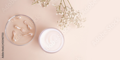 Top view of open box with white cream and cosmetics capsules in petri dish near it.Pastel colors good as mockup large banner.