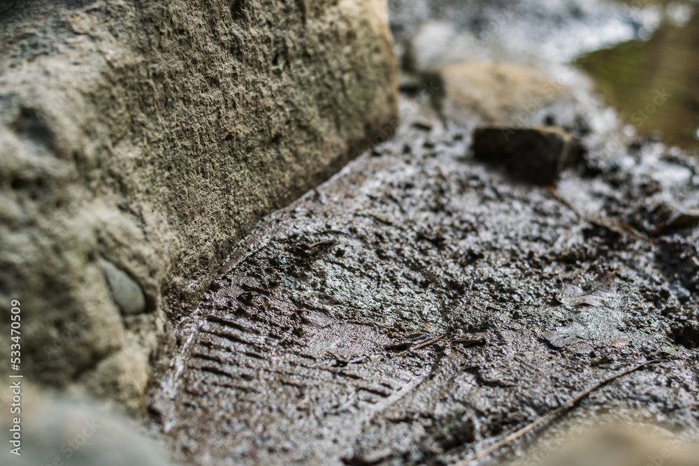shoe print left on a muddy path next to a small stream. looking for the trail. footprint next to a rock. mark of an explorer. hiking concept. shoe print left on a muddy path next to a small stream. looking for the trail. footprint next to a rock. mark of an explorer. hiking concept.