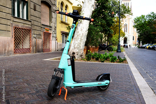 electric scooter parked in vintage style urban walking street. rentable modern, popular means of city or urban transportation. urban lifestyle concept. church building in background. 