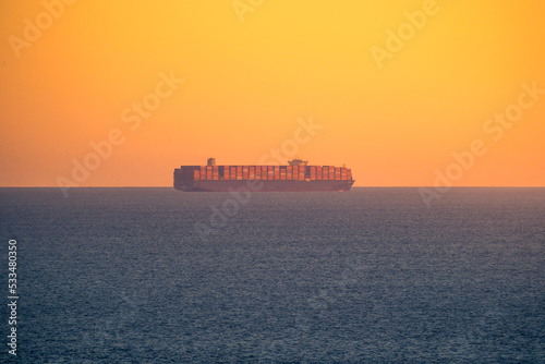 Sailing cargo ship in sea at sunset
