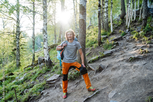 A halt on a mountain road, a guy resting in the forest, summer vacations in the mountains, a hard climb to a mountain peak, orange pants, thick hair, one in the taiga