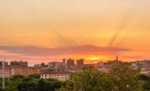 Gorgeous orange-lilac sunset over the city of Piombino, Tuscany, Italy. The rays of the sun pass through the clouds. Gradient sky.