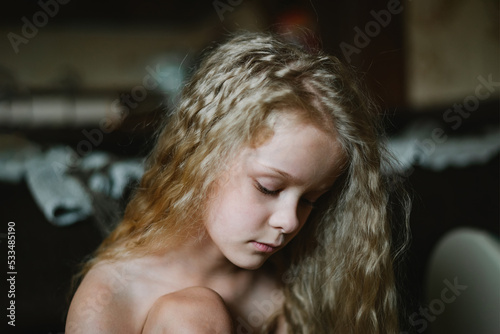 close-up portrait of a pensive, sad little girl with long curly hair at home photo