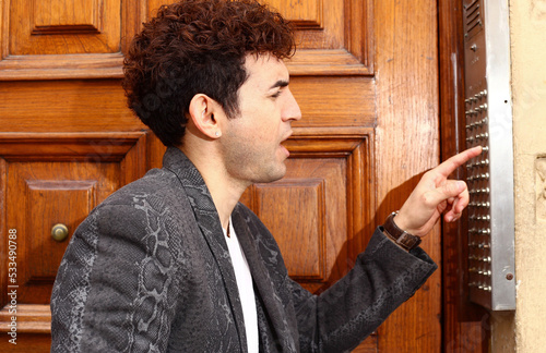 Foto muchacho joven tocando el timbre de una casa de perfil con saco negro y pelo enr